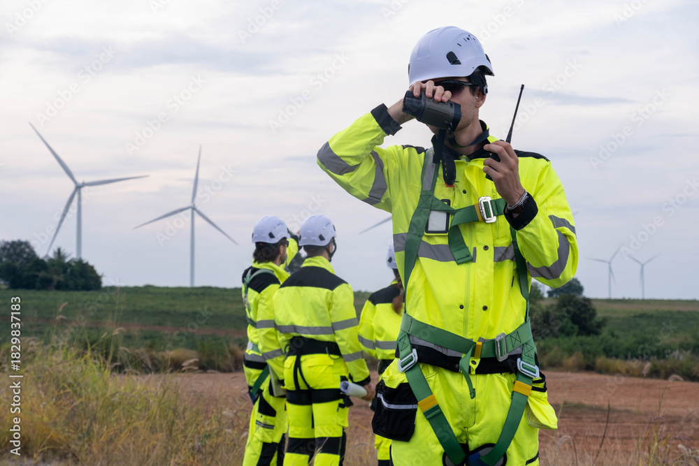 Fototapeta premium Workers in bright yellow safety gear communicate near wind turbines in an outdoor setting