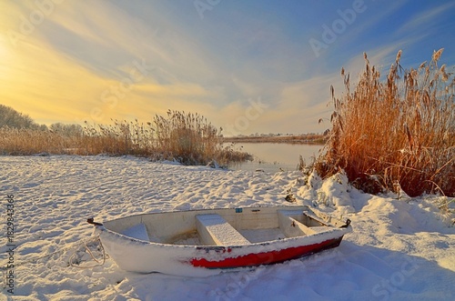 frozen boat on the river at winter sunset