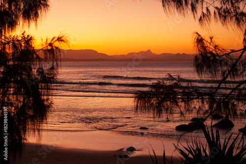 Ausblick auf das Meer und den Strand von Wategos Beach bei Sonnenuntergang. Mt. Warning, Wollumbin im Hintergrund des roten Sonnenuntergangs am Strand.