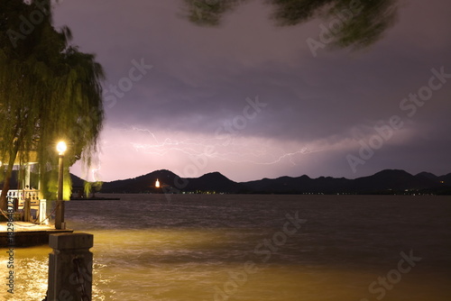 Lightning storm over lakeside with street lights and willow trees