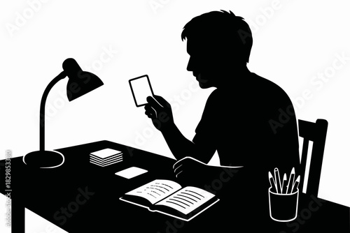Silhouetted figure studies with flashcards, open book and desk lamp in a quiet, organized workspace.