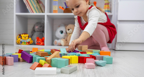 Little girl building a tower with colorful wooden blocks on the floor.