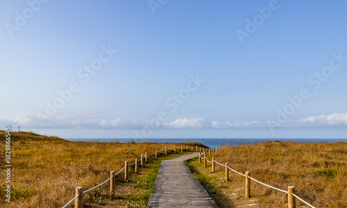 Wooden boardwalk path with rope railing leading to the sea through dunes.