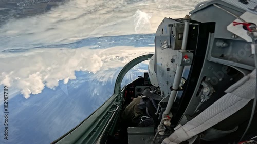 Upside down view from the military fighter jet cockpit performing maneuver, extreme aerobatic flight high in the blue sky above the white fluffy clouds