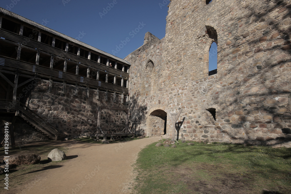 Fototapeta premium Ancient medieval castle courtyard with historic stone fortress walls and a multi-tiered wooden defensive gallery structure under a clear blue sky.