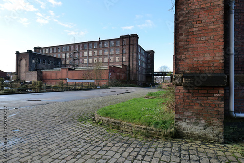 A mill complex with brick exterior. The buildings are set off by a cobblestone parking area.