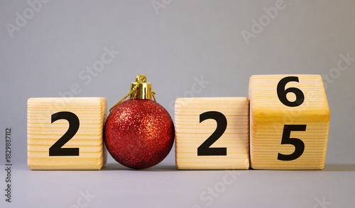 2026 New Year symbol. Businessman turns wooden cube and changes Year 2025 to 2026. Beautiful grey background with Christmas ball. Copy space. Business and 2026 happy new year concept