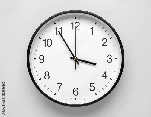 A close-up front view of a simple round analog wall clock with a black frame and white face indicating the time on a light gray wall