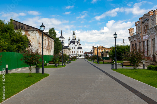 Fototapeta Naklejka Na Ścianę i Meble -  A street in a recreation park in a small Siberian town, bathed in autumn sunshine. At the end of the street is a church. Tourism in Russia