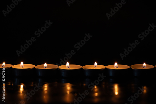 A row of glowing tealight candles against a dark background. Perfect for themes of remembrance, meditation, spirituality, mourning, tranquility, or holiday celebrations.