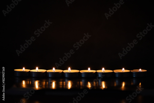 A row of glowing tealight candles against a dark background. Perfect for themes of remembrance, meditation, spirituality, mourning, tranquility, or holiday celebrations.