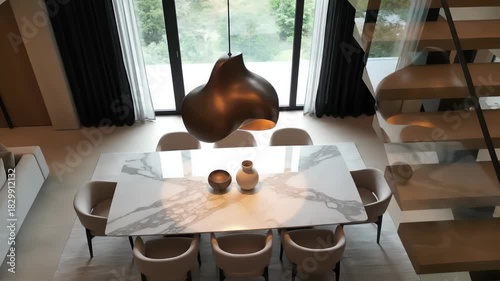A high-angle view of a contemporary dining room featuring a spacious marble-top dining table set with decorative vases and a striking pendant light overhead.