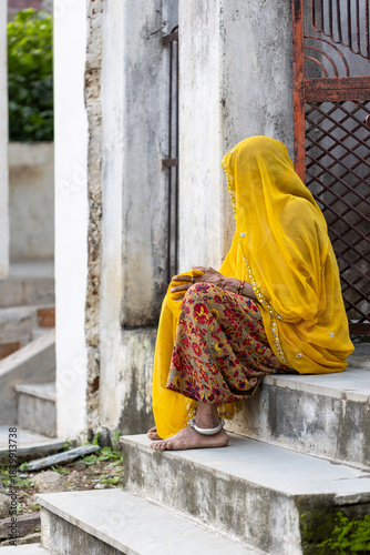 Indian woman dressed in yellow sari sitting at the house entrance