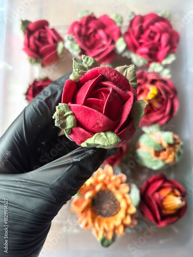 Hand in a rubber glove holding a marshmallow rose, Homemade marshmallow, Marshmallow flowers, Marshmallow roses, tulips and sunflowers are arranged in the background