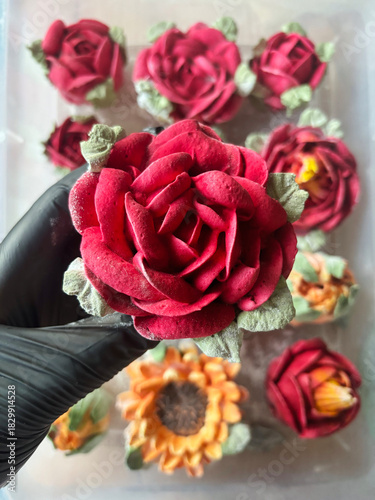 Hand in a rubber glove holding a marshmallow rose, Homemade marshmallow, Marshmallow flowers, Marshmallow roses, tulips and sunflowers are arranged in the background