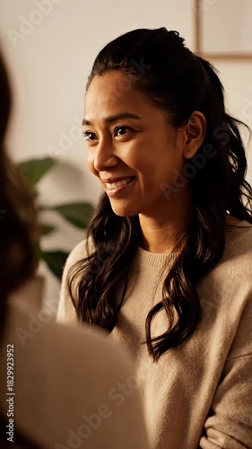 Close up of a radiant young woman with a genuine smile actively engaging in a friendly conversation indoors reflecting happiness and warmth in a cozy atmosphere