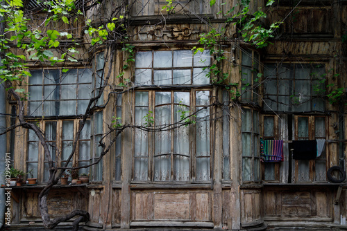 Weathered wooden building facade with large, multi-paned windows, ivy vines, and hanging laundry under soft, diffused daylight.