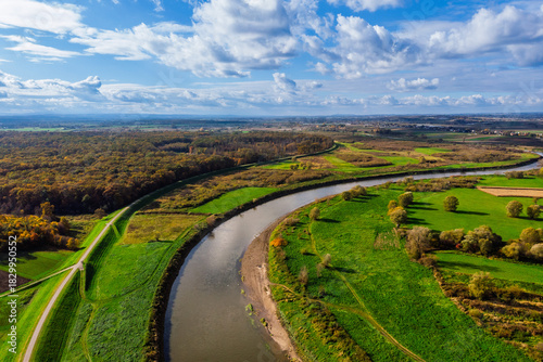 Wide aerial drone view of the Vistula River (Wisła) near Ispina village, Krakow area, Poland. Scenic landscape featuring flood embankments, rural houses, and a cycling route.