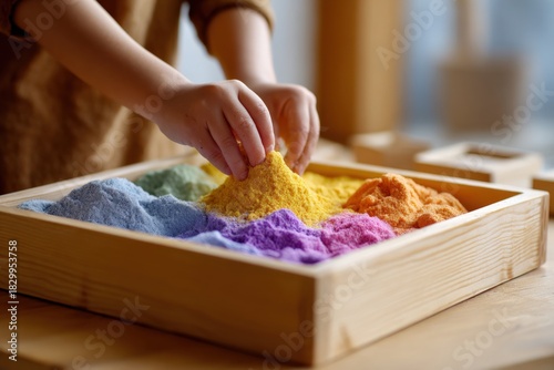 Child's hands playing with colorful sand in a wooden tray
