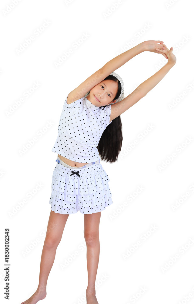 Fototapeta premium Cheerful young Asian girl in polka dot outfit smiles while performing a side stretch, warming up for physical activity on white background.