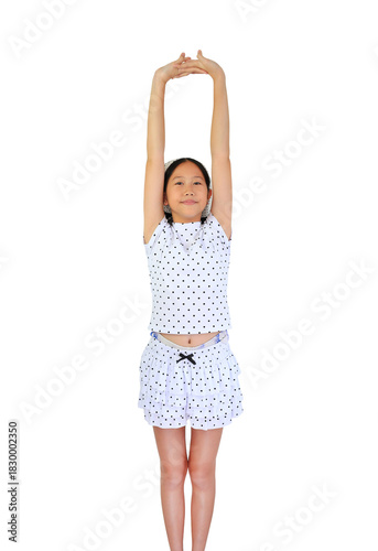 Cute young Asian girl in polka dot stretching her arms up high for stretch or exercise, isolated on a white background.