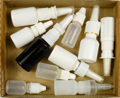 Heap of empty vial of medical drops are in a container for disposal, top view. Treatment and medication concept