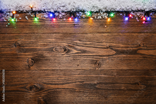 Christmas background featuring a rustic wooden surface decorated with snow and colorful glowing string lights