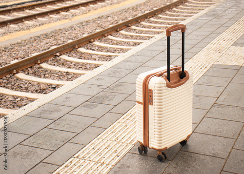 Travel suitcase standing on a train station platform beside railway tracks