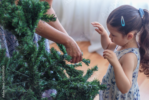 Madre guiando a su hija en la decoración del árbol de navidad