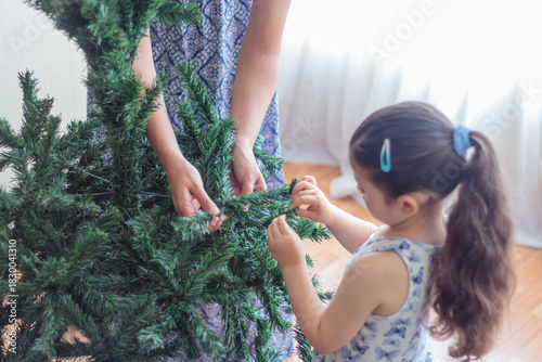 Madre guiando a su hija en la decoración del árbol de navidad