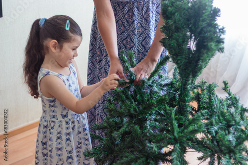 Madre guiando a su hija en la decoración del árbol de navidad