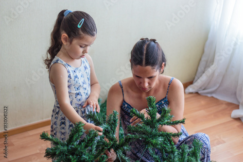 Madre guiando a su hija en la decoración del árbol de navidad