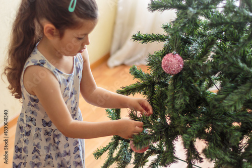 Niña colocando un adorno brillante en el árbol de navidad
