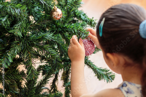 Niña colocando un adorno brillante en el árbol de navidad