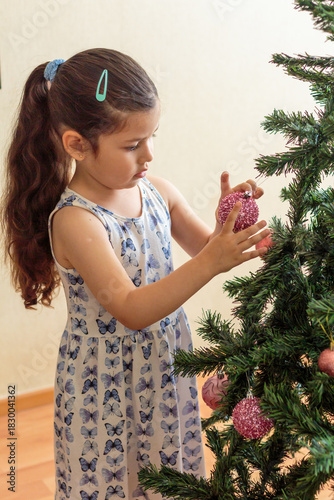 Niña colocando un adorno brillante en el árbol de navidad