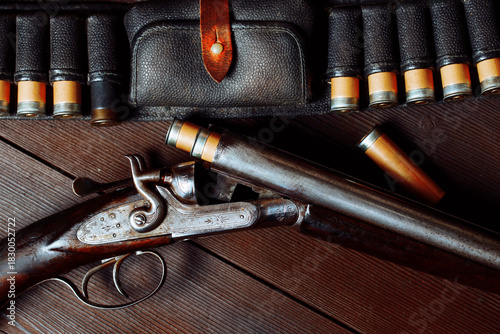 Antique engraved smoothbore rifle lies on a wooden table surrounded by cartridges and a leather case, Hunting concept. 