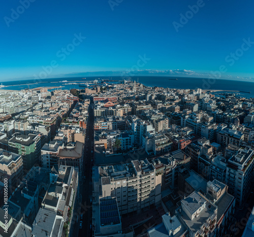 A vibrant aerial panorama of Bari, Italy, capturing the golden-hued Old Town and port alongside the modern city grid, stretching out to the deep blue Adriatic horizon.