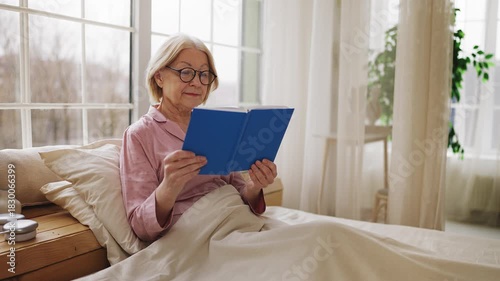 Calm senior woman reading book in bed, relaxing and enjoying leisure time