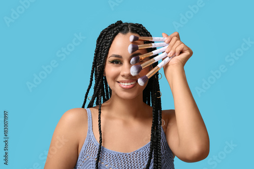 Bild auf Leinwand Young African-American woman with braids and beautiful makeup holding brushes on