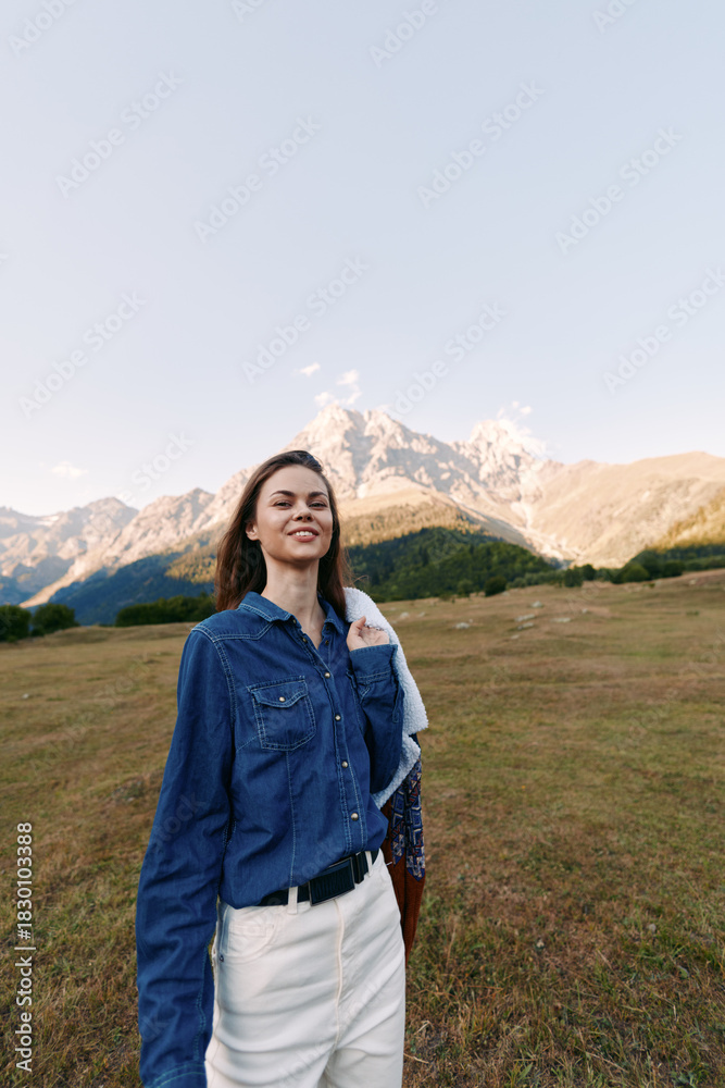 Fototapeta premium Woman smiling in denim shirt portrait in mountain meadow, casual fashion and travel concept. Outdoor lifestyle, scenic landscape and confident young adult enjoying nature.