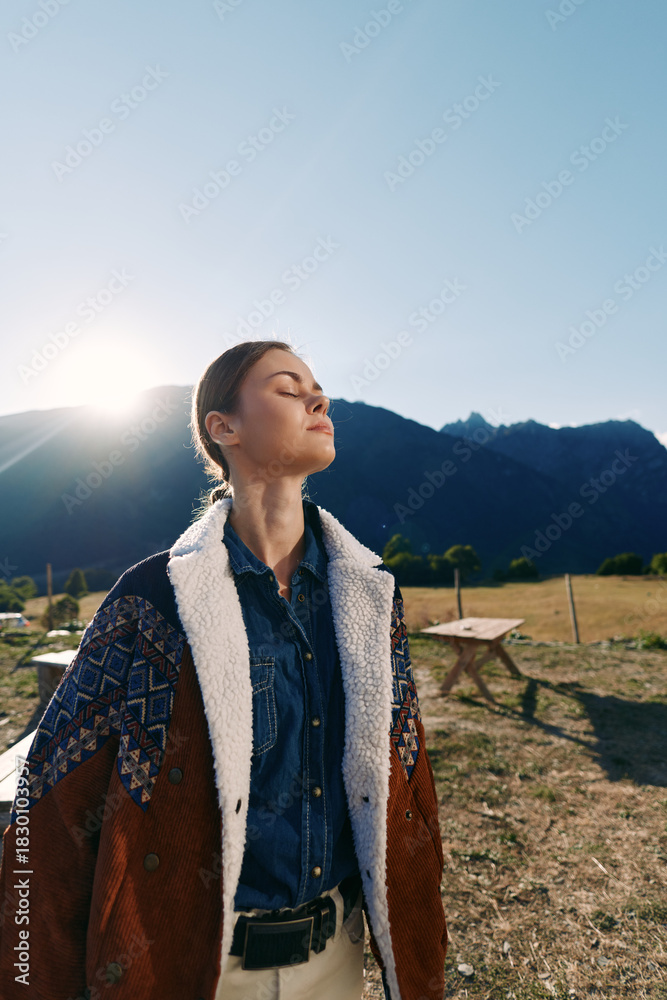 Naklejka premium Woman outdoors in mountains with sunlight on her face, portrait of nature and jacket-clad figure standing peaceful with eyes closed, serene rural lifestyle moment in a meadow.