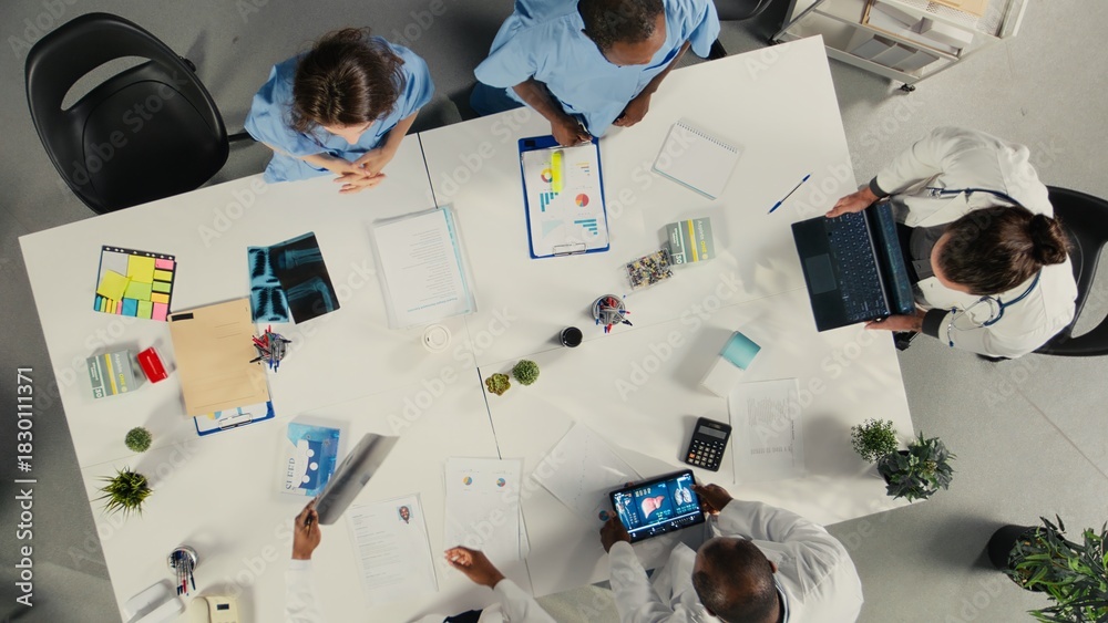Obraz premium Top down view of physicians and medics gathered for briefing conference. Group discusses healthcare advancements, laboratory research and treatment methods to enhance medical care.