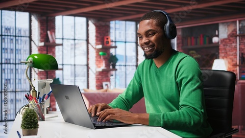 Smiling person in modern loft wearing headphones and listening to music during relaxation time, feeling pleased. Happy guy having fun at home with exciting songs through audio headset. Camera B.