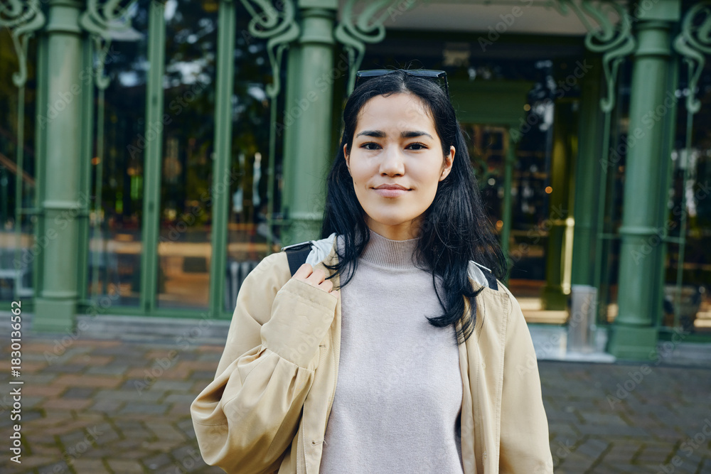 Fototapeta premium Woman outdoors in casual clothing near green architectural columns in daytime urban setting, calm expression, street style and confident vibe, approachable appearance