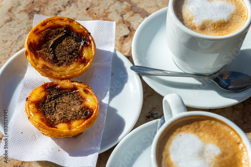 Traditional Portuguese breakfast snack of Pastel de Nata (custard tart) and coffees on a marble counter