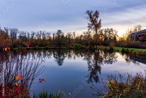 Autumn colored trees stand out along the shoreline and their reflection mirrored in the calm water
