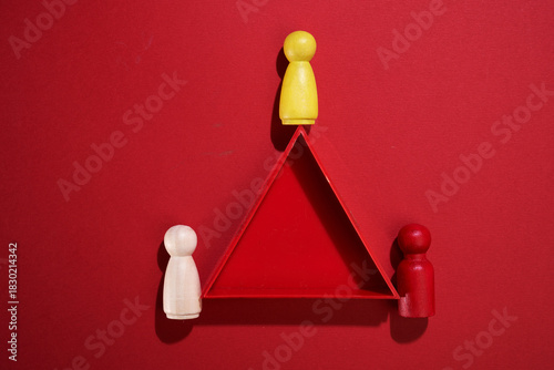 three wood figurines and triangle shape on red background