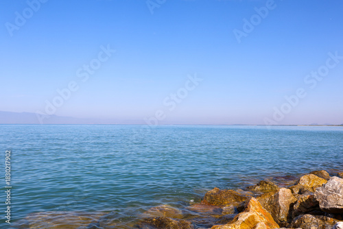 Blue Sky and Calm Water Landscape with Foreground Rocks and Hazy Mountains