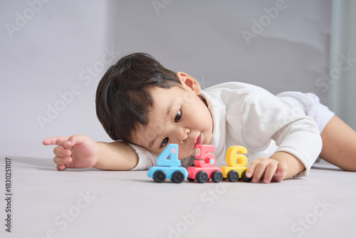 The child lies flat, reaching out to the neatly lined-up toy cars.