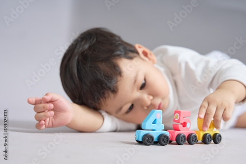 The child lies on the stomach, hands extended toward the colorful cars.
